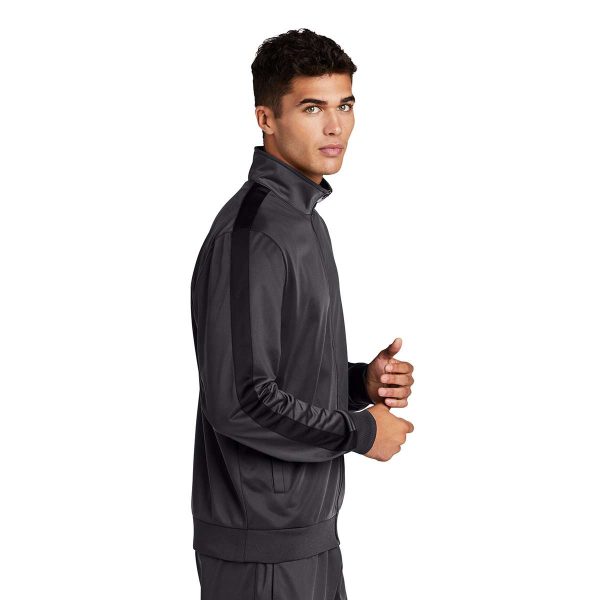 Man posing in a grey Sport-Tek Stripe Tricot Track Jacket with matching pants, side view