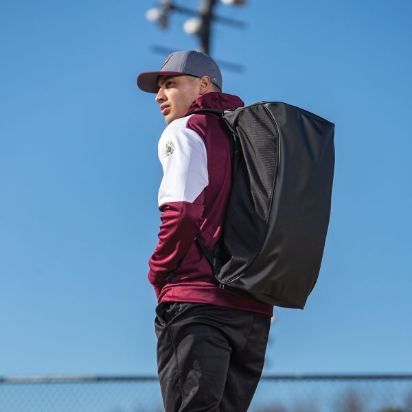 Man wearing on a field with blue sky holding a Holloway Rivalry Backpack Duffel Bag
